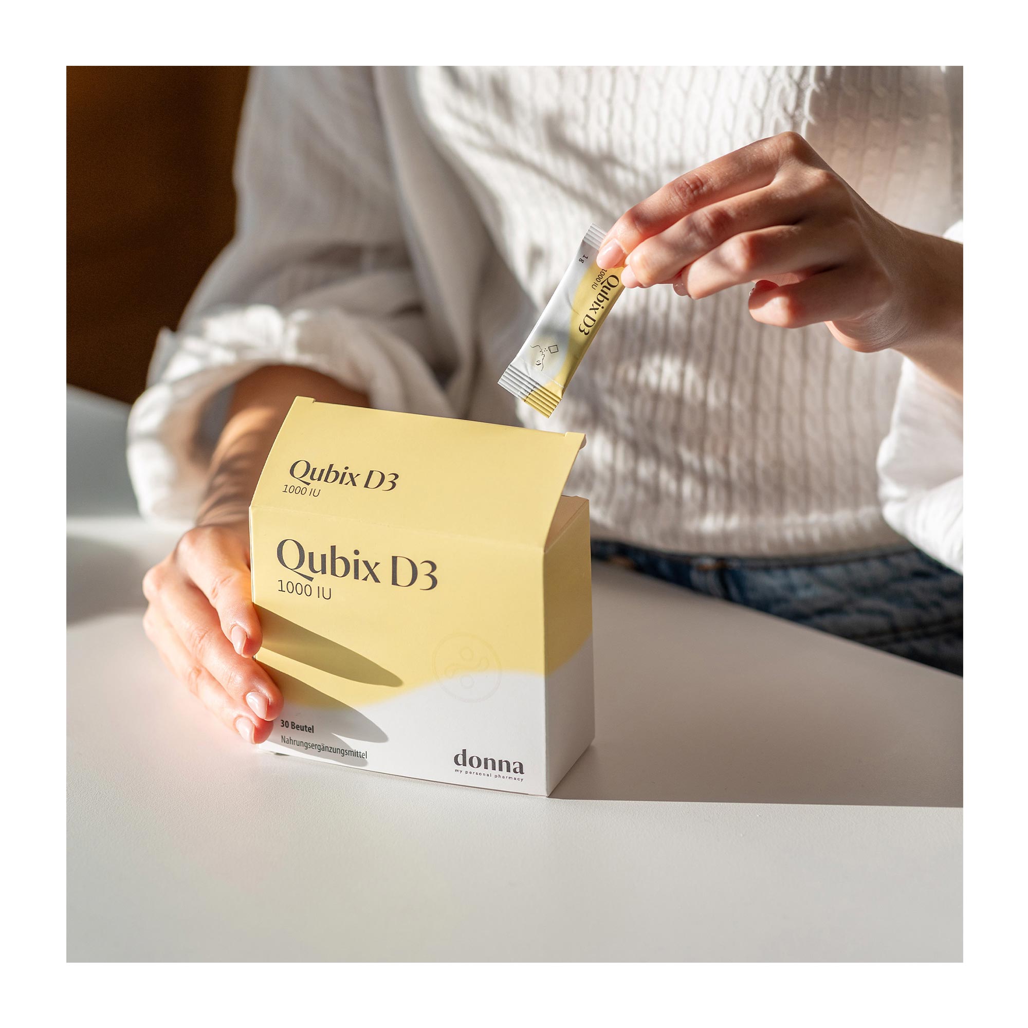 Grafik Qubix Vitamin D3 1000 IU Pulver zum Einnehmen eine Hand entnimmt einen Beutel aus der Verpackung